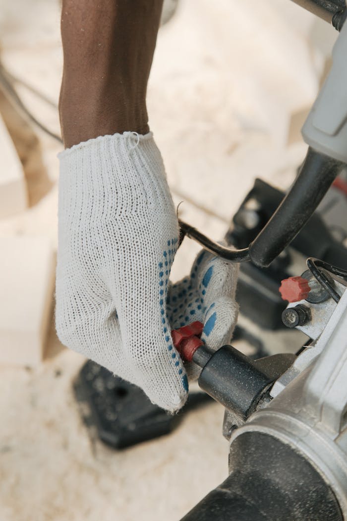 Detailed view of a gloved hand adjusting a saw, emphasizing safety and precision in tools usage.